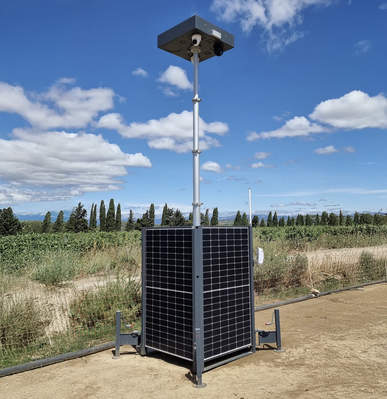 HELIGARD autonomous solar surveillance tower: photovoltaic panels on every face, telescopic mast and cameras, set down in open countryside